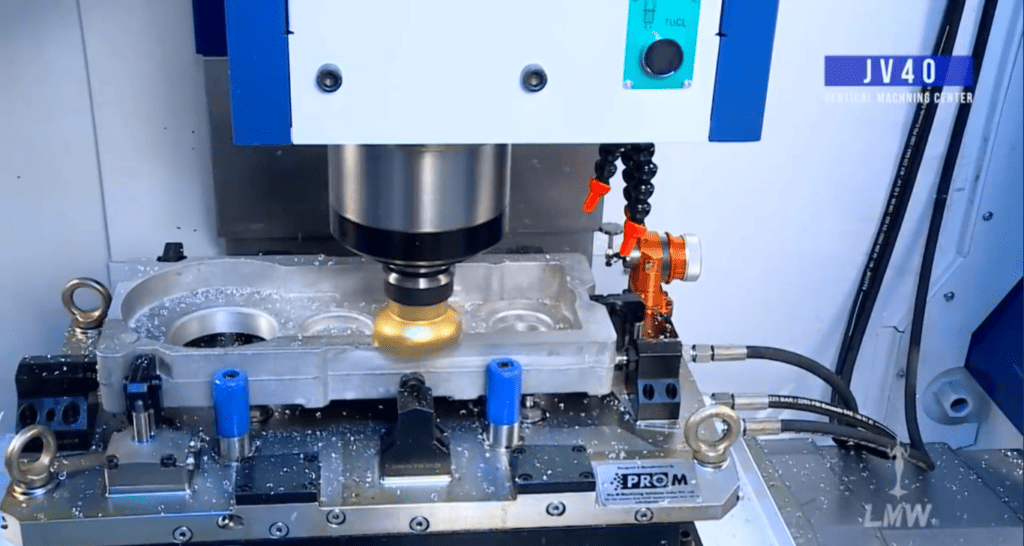 A CNC machine in operation, milling a metallic part with visible metal shavings and a robotic arm nearby.